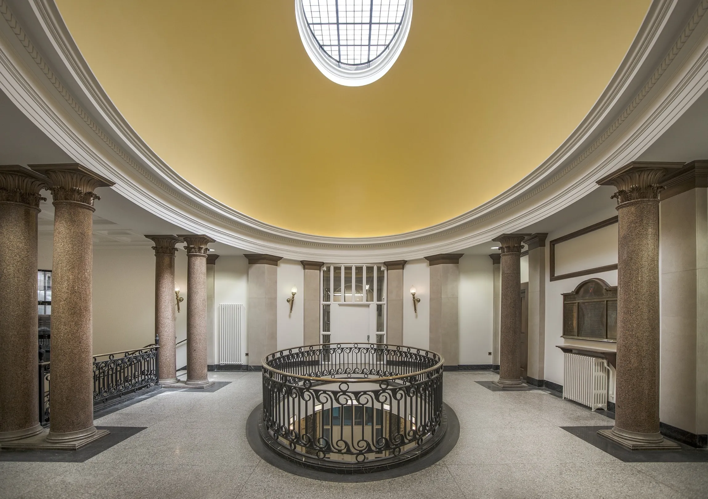 Ornate first floor landing showing central opening to view the floor below and a large domed ceiling with skylight. Marble pillars support the dome.