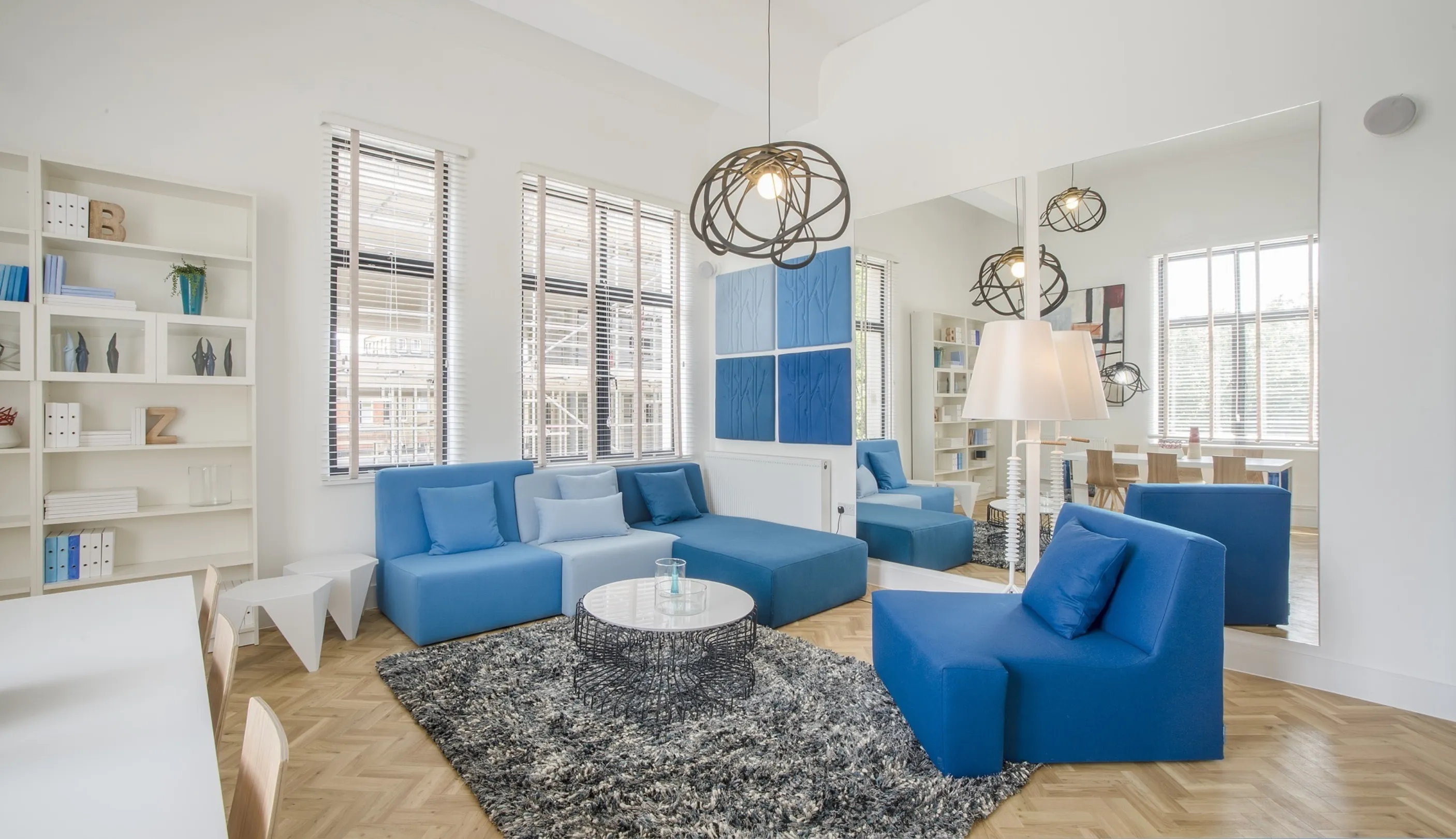 Modern interior living space with designer furniture throughout, large mirrors and parquet floor.