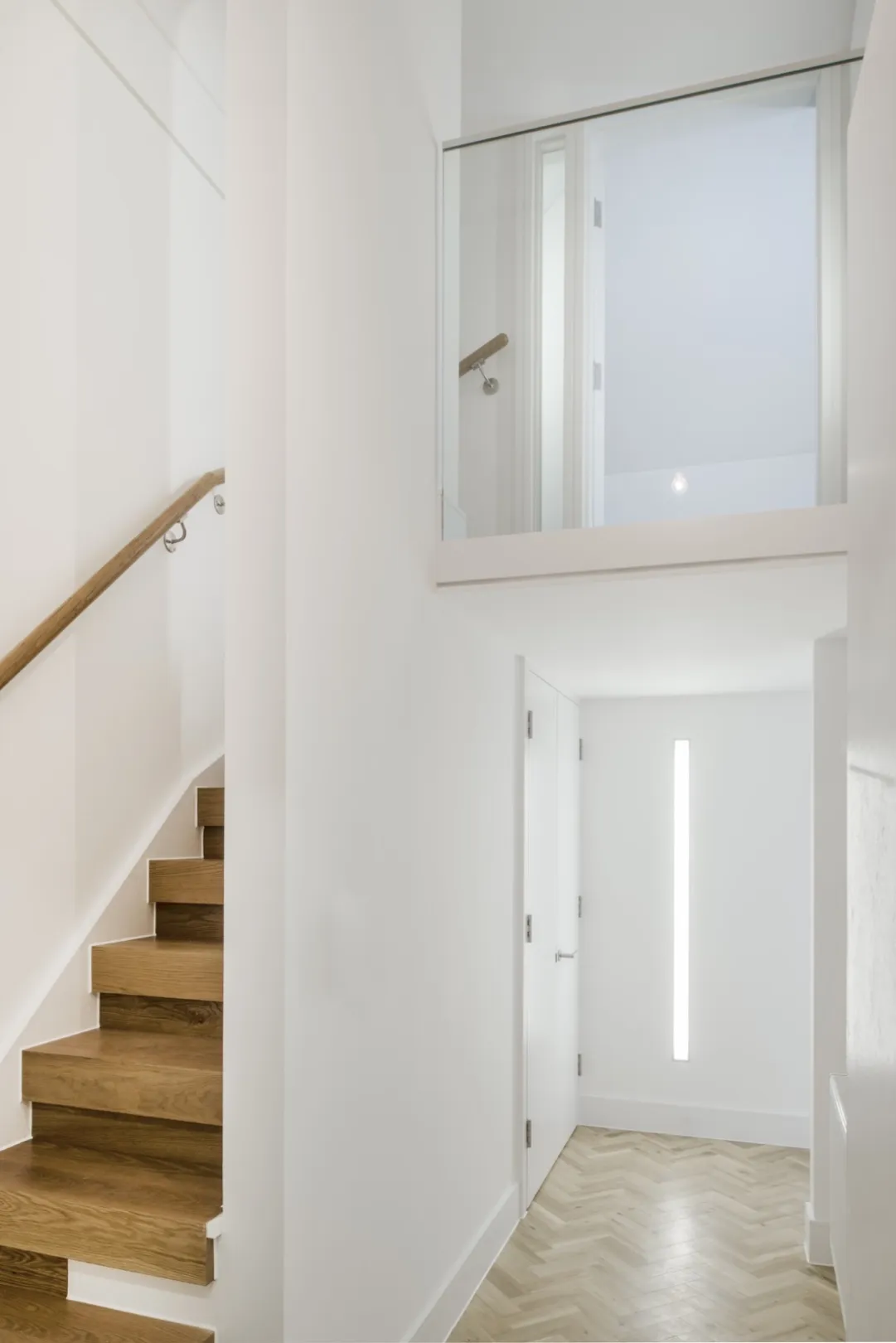 Modern interior living space showing split level with glazed balustrade, parquet floor and chunky wooden staircase.