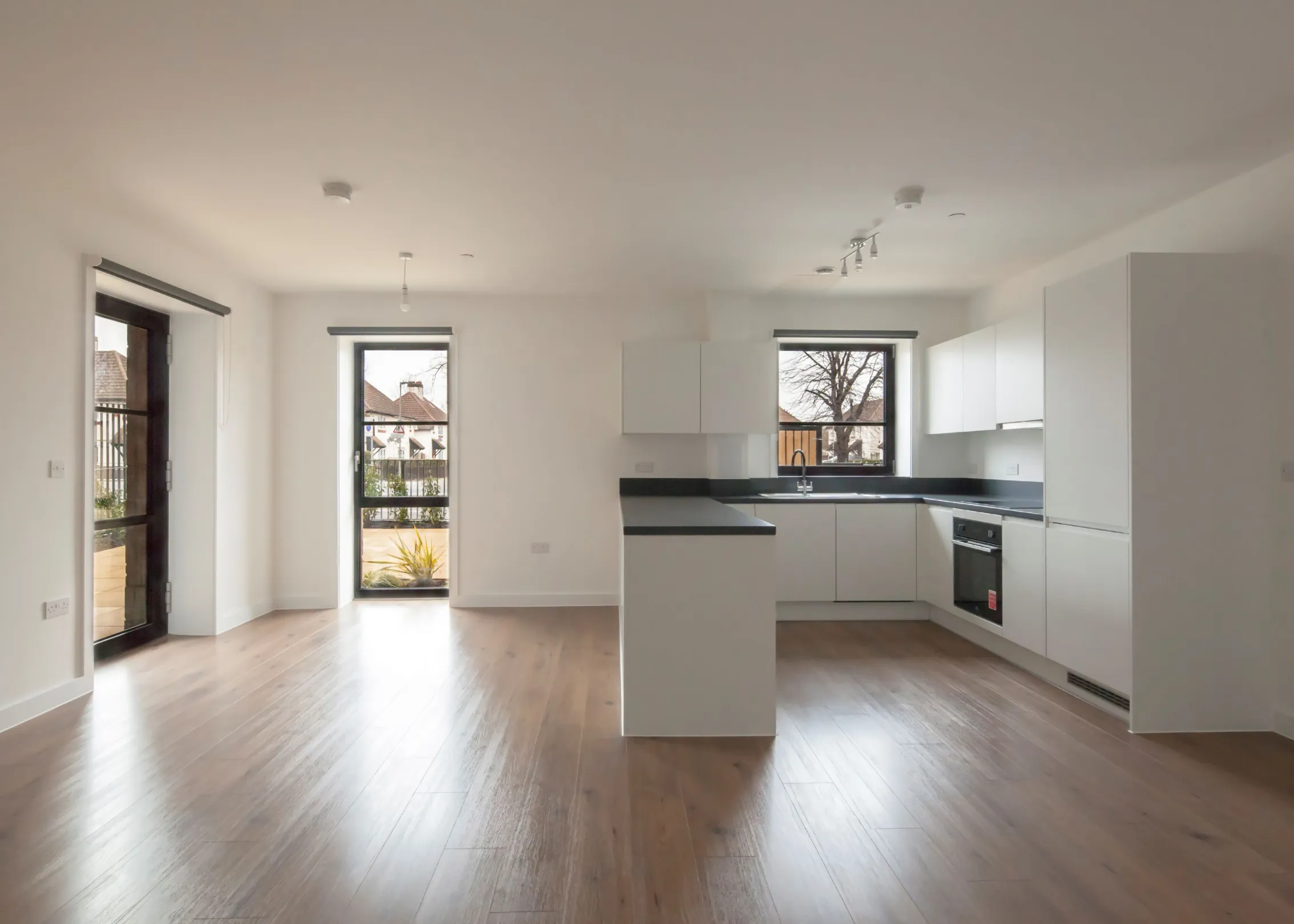 A new build kitchen and living room. Kitchen is white with handleless cupboards and integrated appliances.  Flooring is laminate wood effect.  Large floor to ceiling windows.