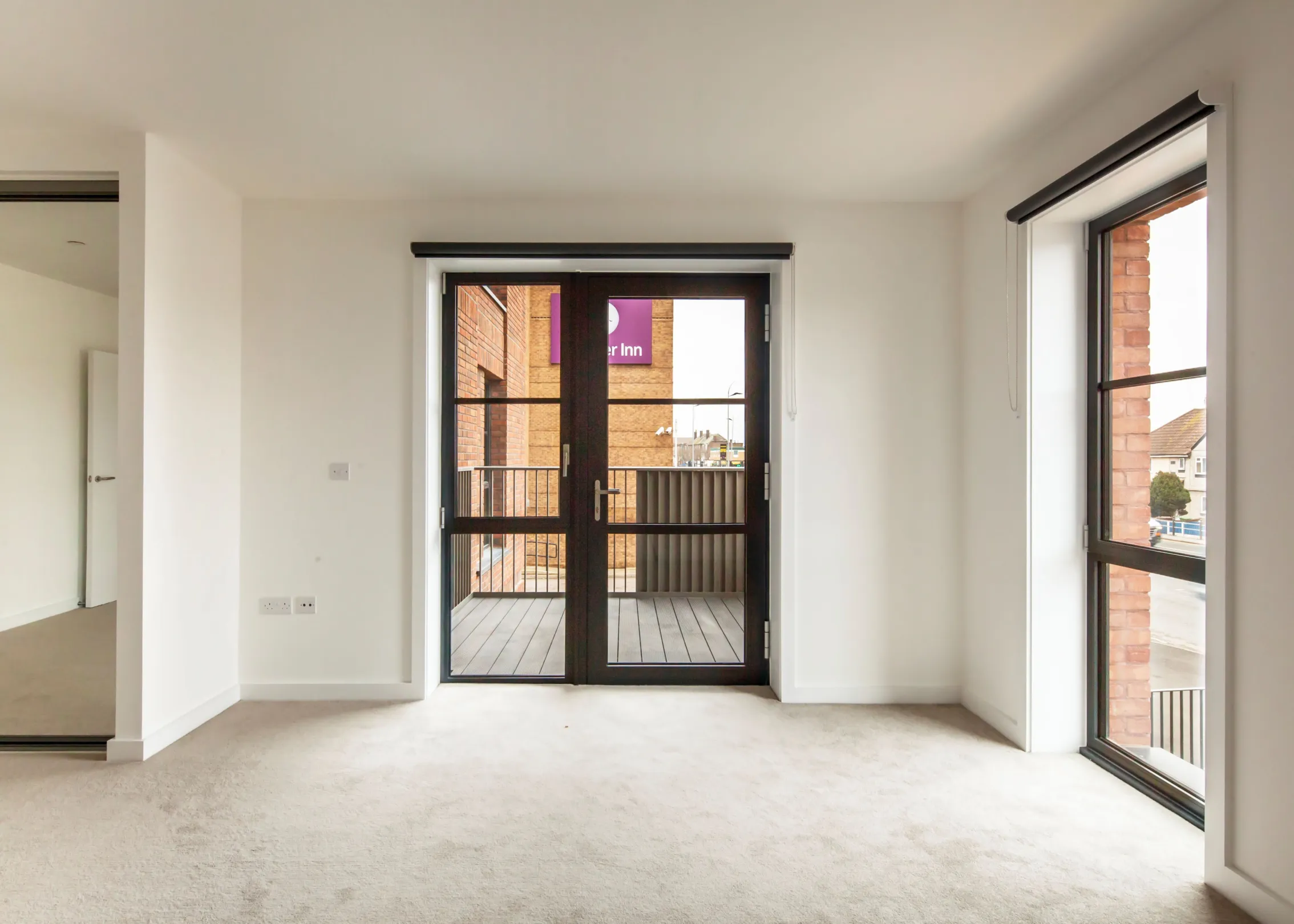 A bedroom in a new development, grey coloured carpet, sliding door wardrobe with mirrors and floor to ceiling height windows.  A glass balcony door leading to the balcony.