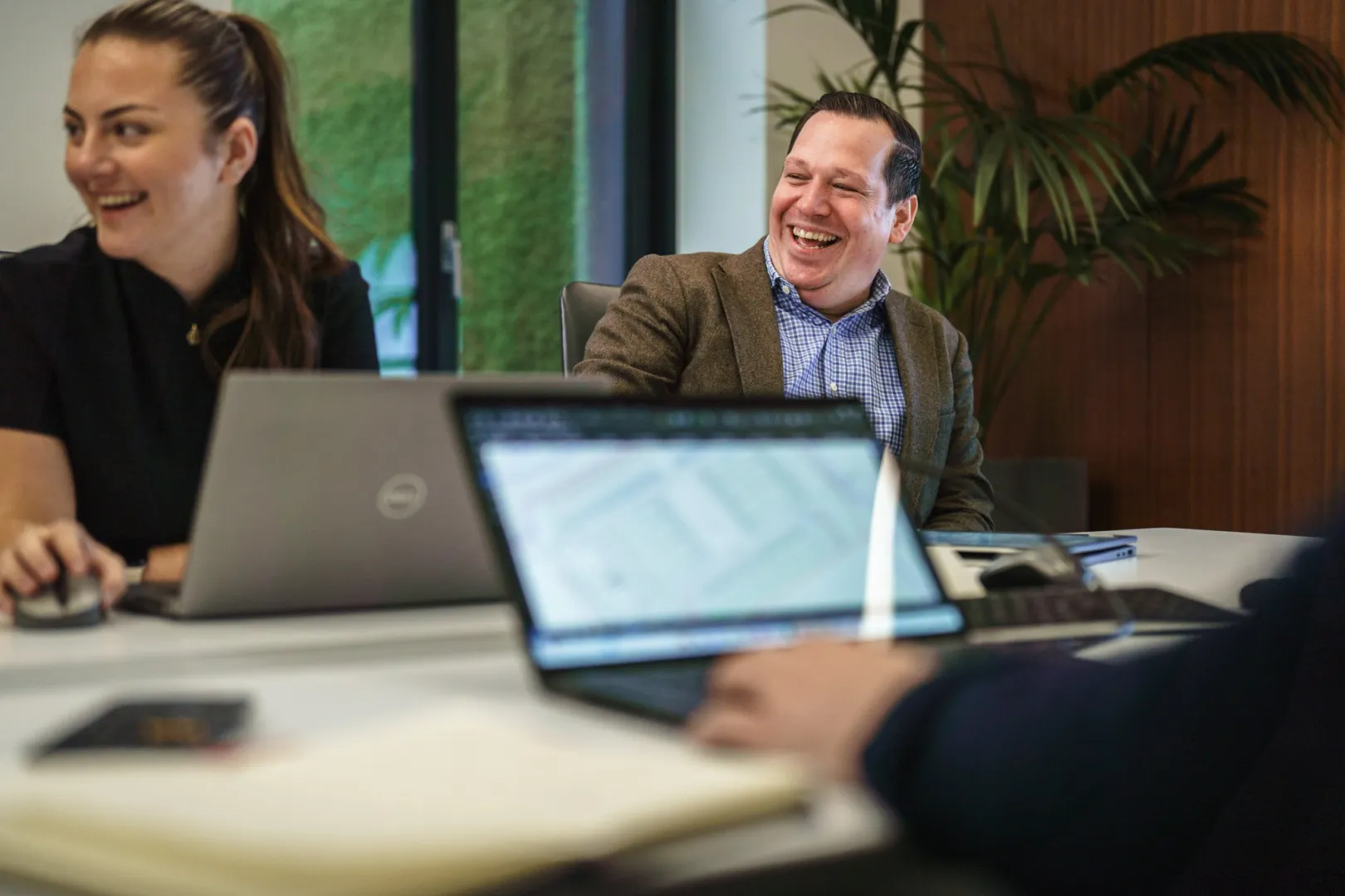 Man and women sit at a board room table in front of open laptops
