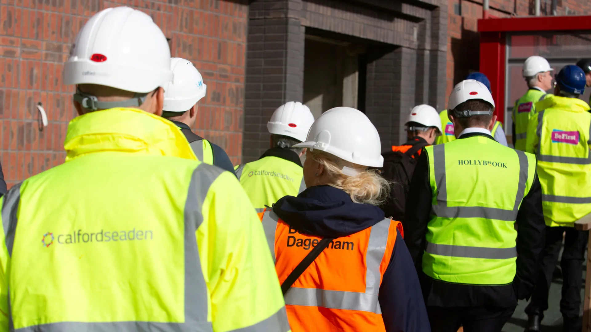 Group of people on a building site wearing high viz jackets and hard hats getting into a hoise